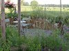 Kiesplatz mit Bistrotisch und zwei Stühlen, umgeben von blühenden Wildstauden und einer rostroten Stahleinfassung