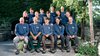 Das Team von Kunz Gärten in blauen Firmenpullovern, in zwei Reihen vor einer Hecke